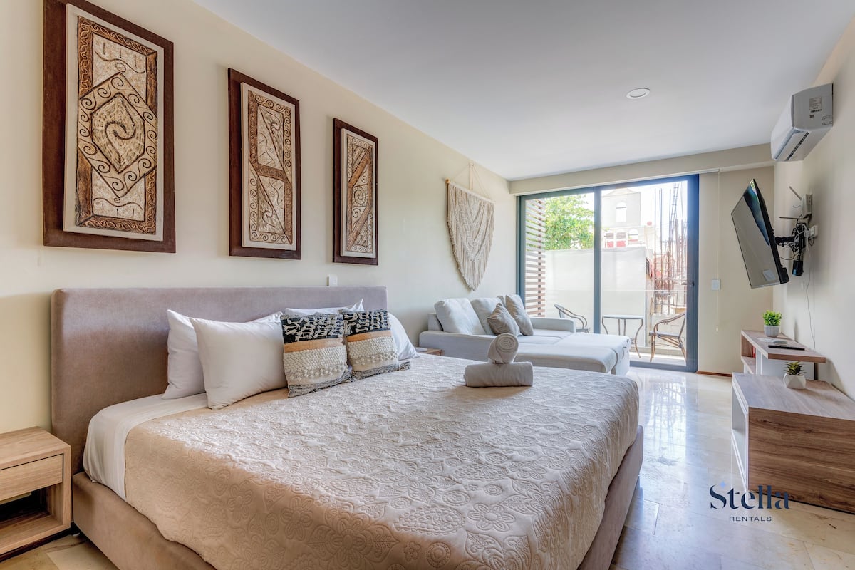 A bedroom with a large bed, a sofa, a TV, and a balcony.