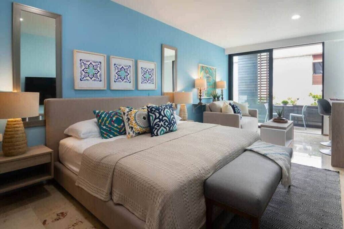 A hotel room with a large bed, a nightstand with a lamp, a bedside table, and a view of the outside balcony.