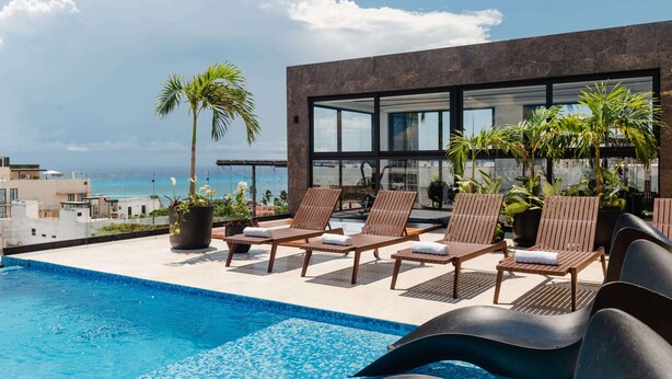 A rooftop pool area with lounge chairs and potted plants, overlooking a cityscape and the ocean. - Apartments near 5th Avenue with Rooftop Ocean View (Playa del Carmen)