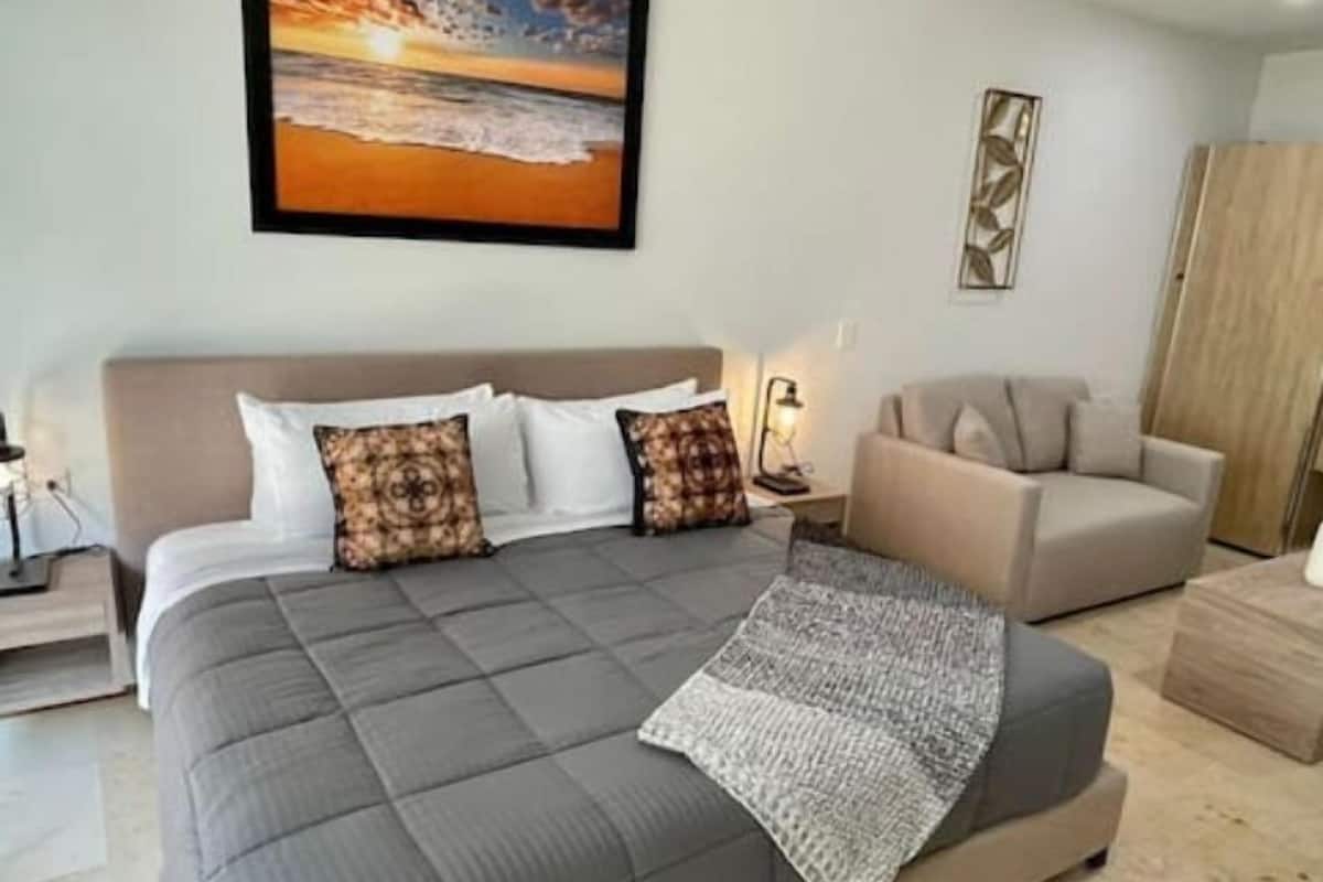 A bedroom with a large bed, a sofa, a nightstand, and a painting on the wall.