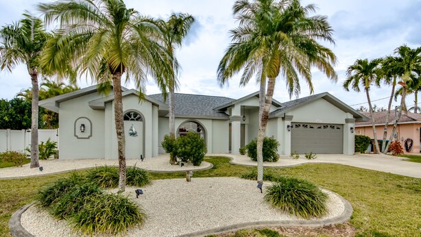 A two-story house with a garage, surrounded by a landscaped garden with palm trees and a gravel driveway. - New to VRBO, Pelican Way, Heated Private Pool, Large Lanai area, Billiards..... (Cape Coral)