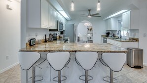 A modern kitchen with white cabinets, a granite countertop, and four bar stools. - New to VRBO, Pelican Way, Heated Private Pool, Large Lanai area, Billiards..... (Cape Coral)