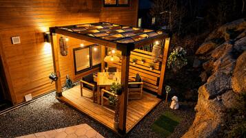Una terraza de madera con una pérgola, mobiliario y plantas en macetas.