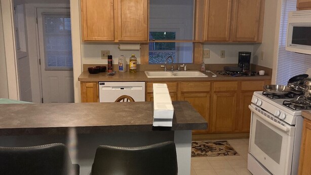 A kitchen with wooden cabinets, a stove, a sink, and two bar stools. - Private stand-alone little house.   (Fairview Park)