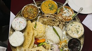 Een traditionele Indiase maaltijd met diverse gerechten, waaronder rijst, platbrood en meerdere currys, gepresenteerd op een metalen dienblad.