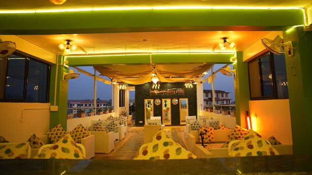 Een restaurant met een groen-wit kleurenschema, met een centraal zitgedeelte met ronde tafels en stoelen, en een uitzicht op de stadsachtergrond.