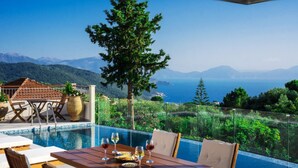 Ein Poolbereich mit Esstisch, mit Blick auf eine Berglandschaft und das Meer.