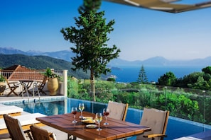 Ein Poolbereich mit Esstisch, mit Blick auf eine Berglandschaft und das Meer.