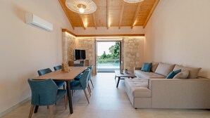 Ein modernes Wohnzimmer mit Holzbalkendecke, Steinwand, einer Couch und einem Essbereich mit Stühlen.