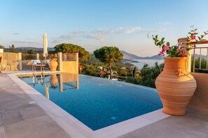 An infinity pool with a view of the sea and mountains, surrounded by outdoor furniture and potted plants. - Pithari Sunset Villa (Kefalonia)