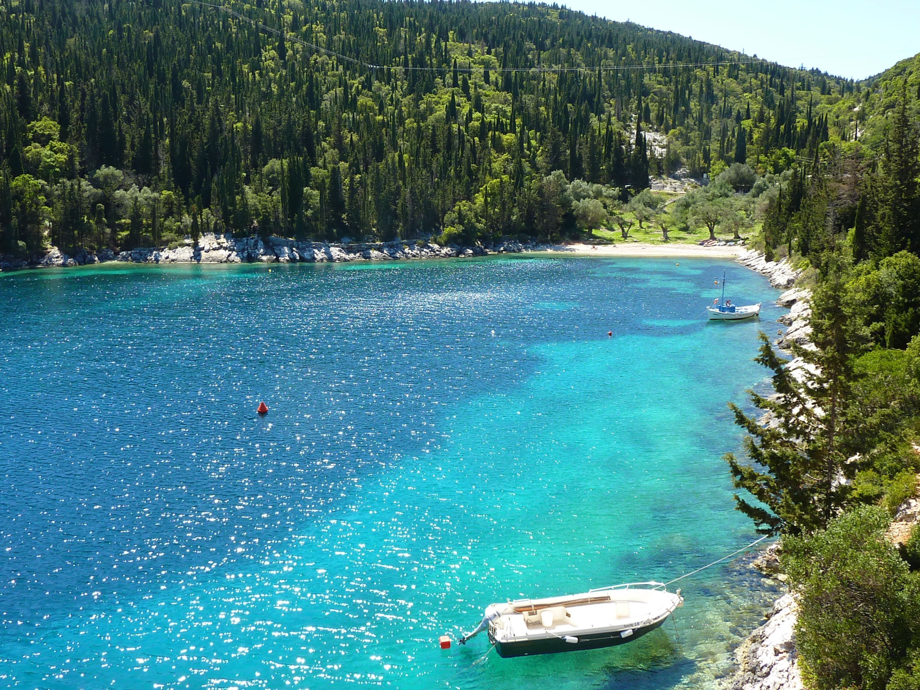 Um barco ancorado em um mar azul-turquesa cristalino, com uma costa arborizada.