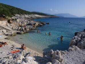 A rocky beach with clear water, people swimming and sunbathing, and a mountainous backdrop. - Pithari Sunset Villa (Kefalonia)