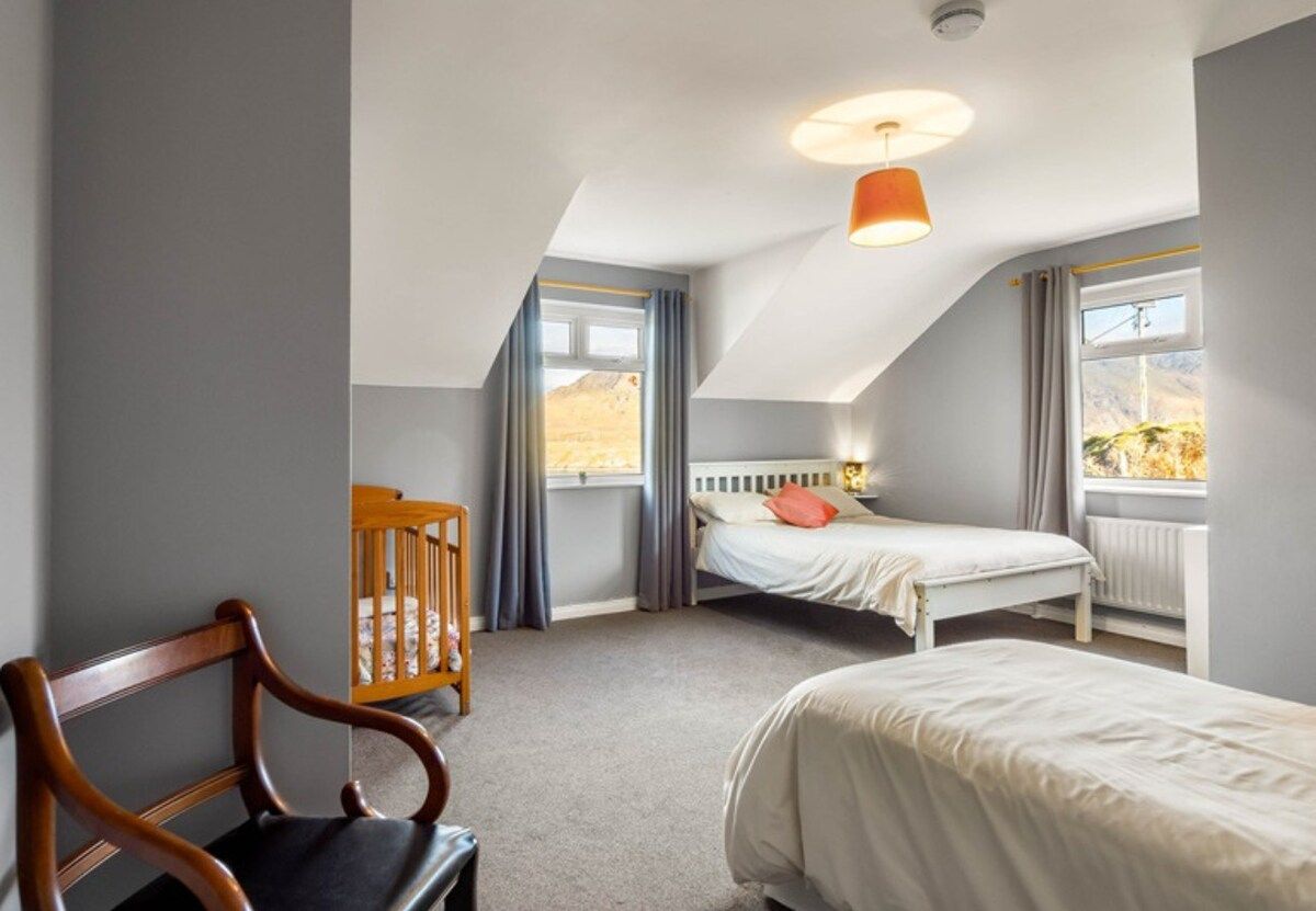 Une chambre avec un plafond en pente, un lit, une chaise et une fenêtre donnant sur un beau paysage.