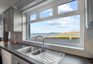 A kitchen with a large window overlooking a coastal landscape. - Glassillaun Beach House (Renvyle)
