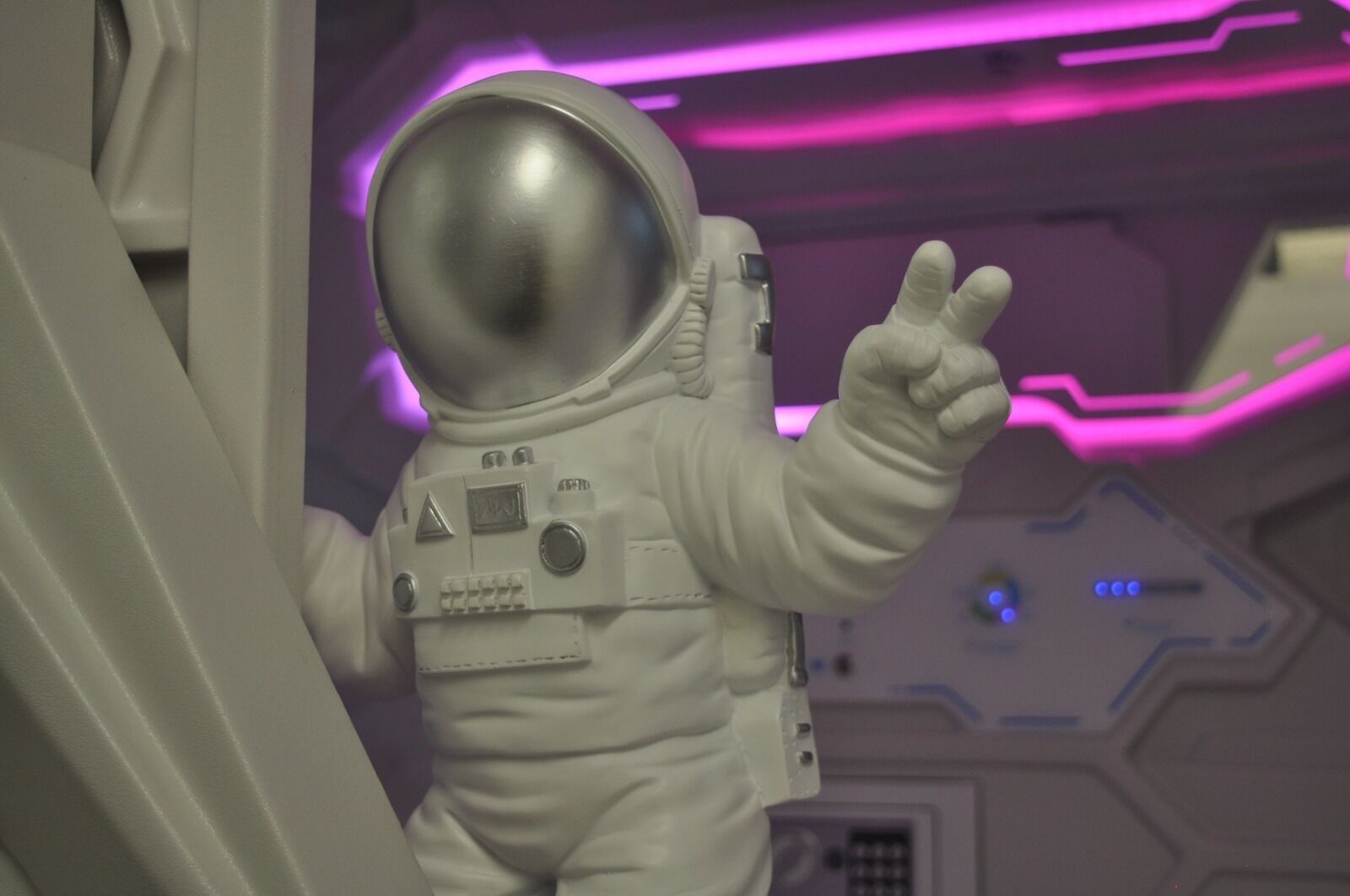 Un traje espacial con casco, un gesto con la mano y un interior futurista con iluminación púrpura.
