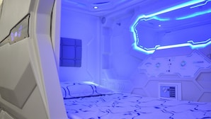 A futuristic room with a bed, control panels, and a blue-lit ceiling. - Cosmos capsule coworking hub London (London)