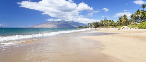 A beach with clear skies, calm waters, and a mountain in the background.