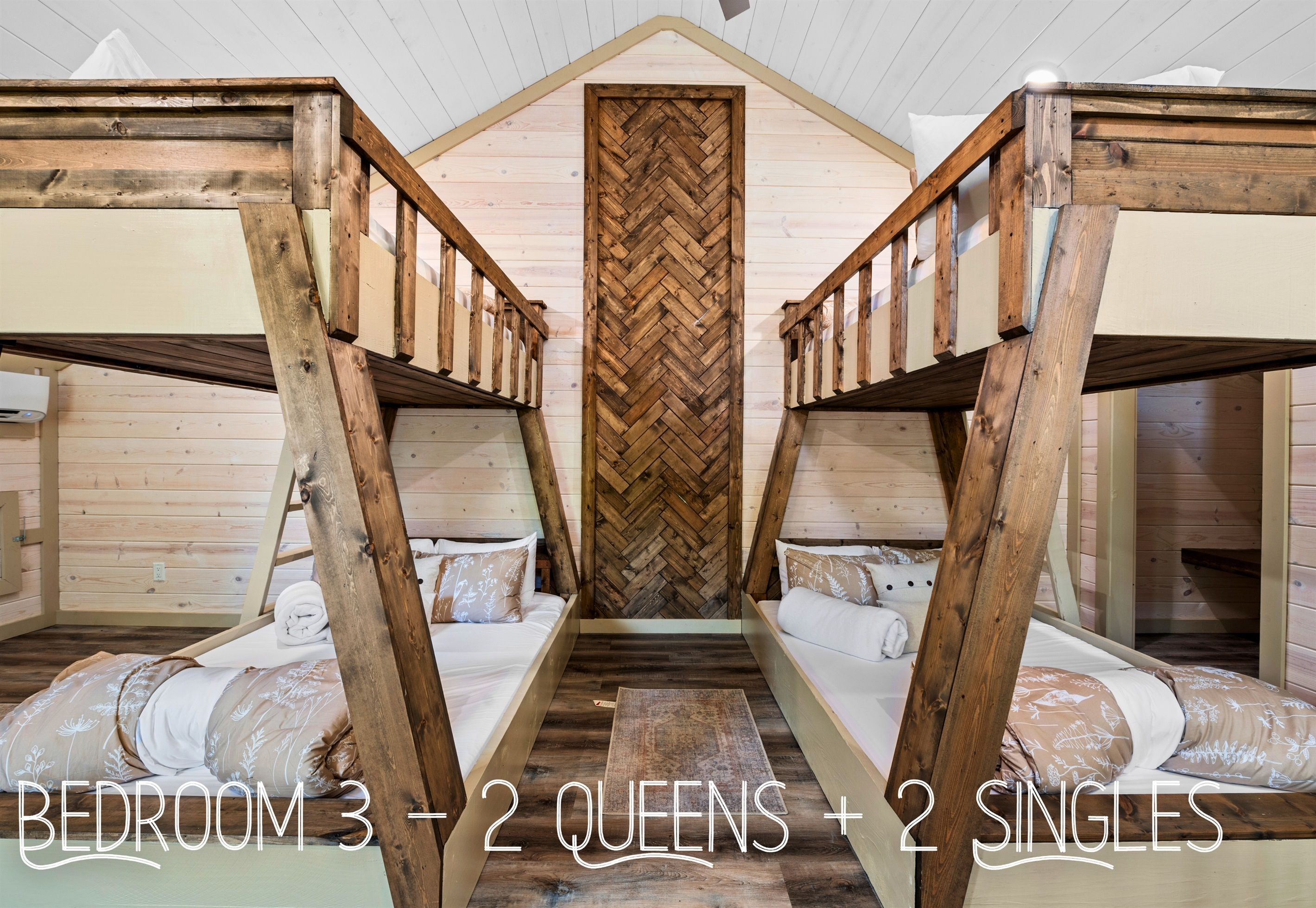 A bedroom with three beds, two queen-sized and two single beds, arranged in a symmetrical layout with a herringbone-patterned wall in the center.