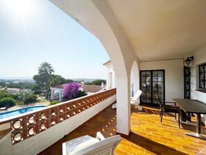 A balcony with a view of a swimming pool, a table, and chairs.