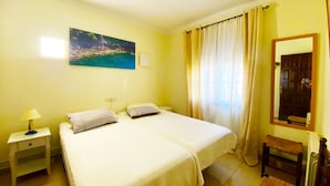 A room with a bed, a nightstand, a chair, a painting, and a window with curtains.