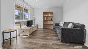 Moderni olohuone, jossa on harmaa sohva, puinen TV-taso ja kirjahylly.