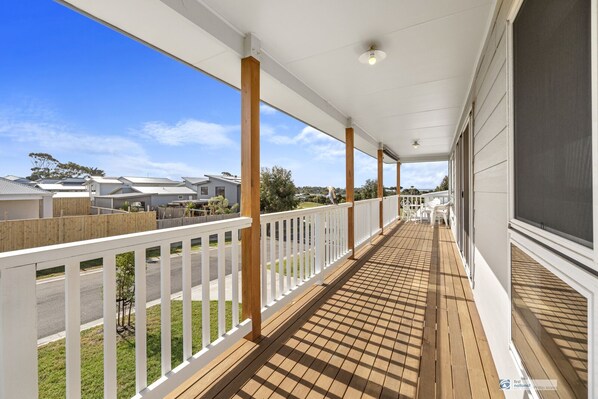 A covered porch with a wooden deck, white railings, and a view of a residential street. - Cadwell Comfort, family holiday retreat (Cowes)