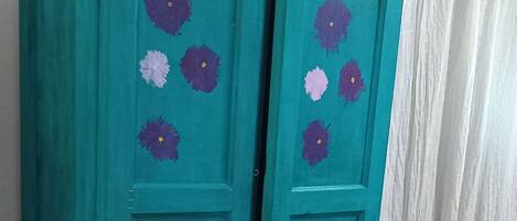 A teal dresser with floral patterns and a bed with a blue headboard in the background.