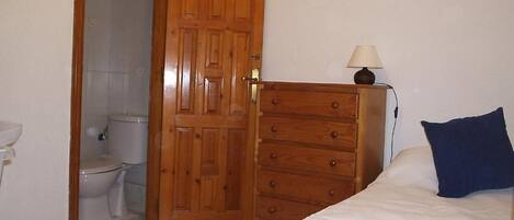 A bedroom with a wooden wardrobe, a bed with a blue pillow, and a nightstand with a lamp.