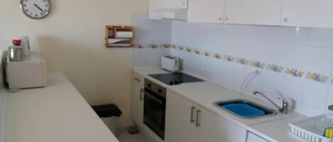 A compact kitchen with white cabinets, a built-in oven, a sink, and a washing machine.