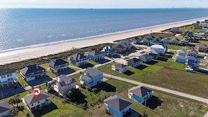 Vista aérea de una zona residencial costera con casas, una playa y un cielo despejado.