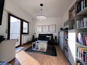 Een moderne woonkamer met een bank, salontafel, boekenkast en kunstwerk aan de muur.