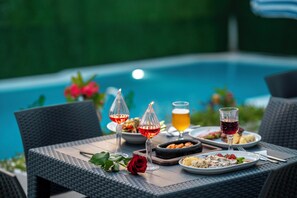 A dining table with plates of food, wine glasses, and a bowl of snacks by a poolside. - Kemer Royal Beach Hotel (Kemer)