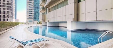 A swimming pool area with lounge chairs and a modern building in the background.