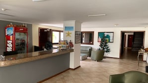 A reception area with a counter, a refrigerator, a Christmas tree, and a green armchair. - Pousada Maristella (Salvador)