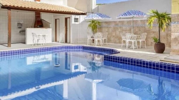 A swimming pool with a tiled edge, surrounded by outdoor furniture and umbrellas. - Pousada Maristella (Salvador)