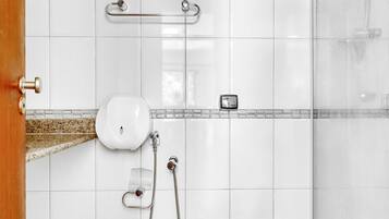 A bathroom with white tiles, a shower, a toilet, and a handrail.