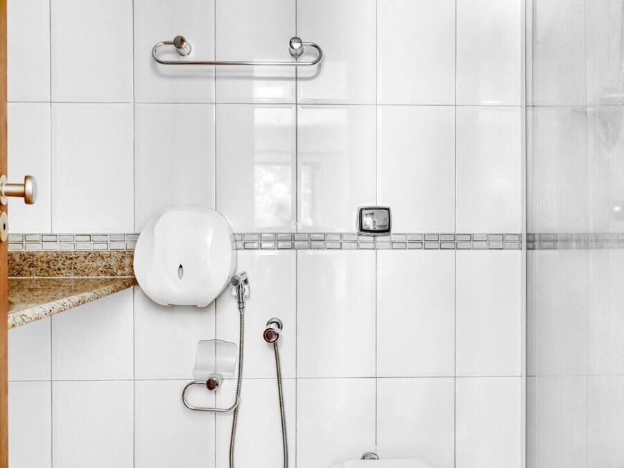 A bathroom with white tiles, a shower, a toilet, and a handrail.