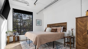 Ein Schlafzimmer mit großem Fenster, einem Bett mit Holz Kopfteil, einem Nachttisch, einem Holzschrank und einem gemusterten Teppich.
