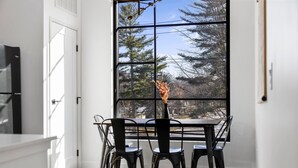 Ein Essbereich mit Tisch und Stühlen, ein Fenster mit Blick auf Bäume und eine Tür.