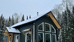 Une cabane à l’extérieur sombre, dotée de grandes fenêtres et d’un toit en pente.