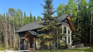 Un chalet doté d’une cheminée en pierre et de chaises Adirondack rouges dans la cour.