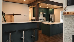 Une cuisine moderne avec des meubles de couleur sombre, un plafond en bois et un coin bar équipé de tabourets.