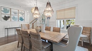 A dining area with a large wooden table, wicker chairs, and hanging crystal chandeliers. - "Seaglass" Watersound home with Golf Cart, Pool, and Private Beach (Santa Rosa Beach)