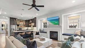 A modern living room with a fireplace, a large TV, and a ceiling fan. - "Seaglass" Watersound home with Golf Cart, Pool, and Private Beach (Santa Rosa Beach)