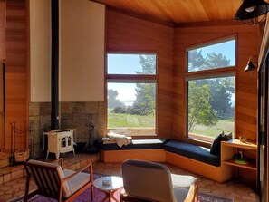 A cozy cabin interior with a stone fireplace, a bench with a cushion, and a view of the outdoors.
