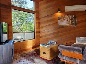 Ein gemütliches Blockhaus-Interieur mit großem Fenster, Fernseher, Sofa und kleinem Holzkasten.