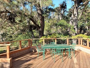 A wooden deck with a green metal table and chairs, surrounded by trees.