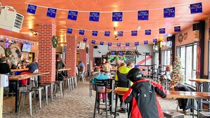 A restaurant with multiple tables and chairs, a brick wall, and hanging blue banners.