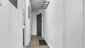 A narrow hallway with white walls and wooden flooring, leading to a dark door at the end.