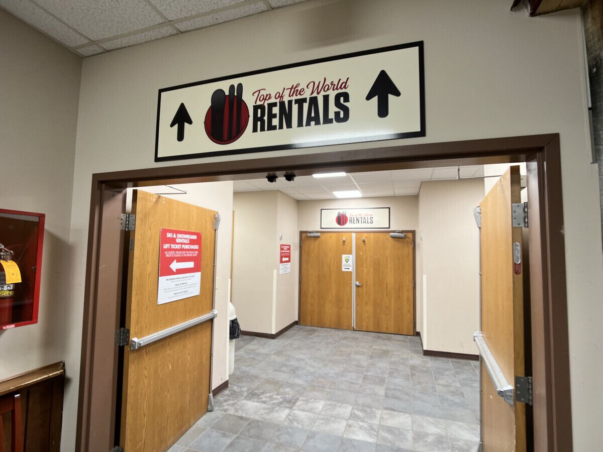 Un couloir avec une enseigne indiquant « Top of the World Rentals » et une autre indiquant « Vente de forfaits de remontées mécaniques ».